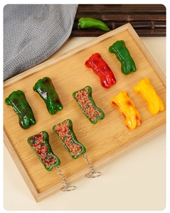 Close-up of realistic PVC stuffed green chili and pepper keychains on a wooden tray