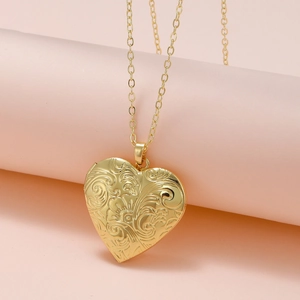 Close-up of golden heart locket necklace with intricate floral engravings on pink background