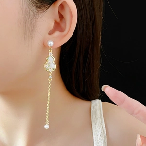 Detailed view of long gourd flower earrings with pearls and gold chain on a model