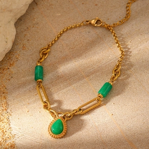 Detailed close-up of gold chain bracelet with green stone charms on a sandy stone background