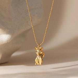 Close-up of a gold-plated cat pendant with rhinestone eyes on a beaded bead chain