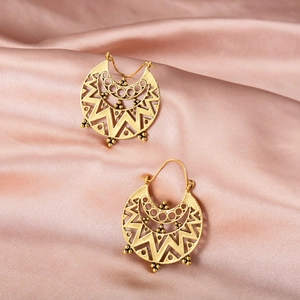 Macro shot of vintage gold hollow-carved geometric earrings on silk fabric texture
