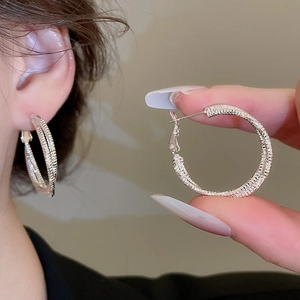 Close-up of textured silver hoop earrings with diamond-cut finish and hinge closure