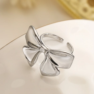 Macro shot of silver bow knot open ring with high-polish metallic texture on beige backdrop