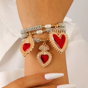 Detail eines mehrlagigen Perlenarmband-Sets mit roten Herzanhängern in Barock-Goldfassung