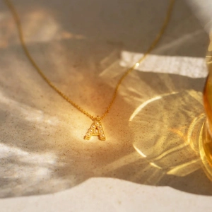 Macro shot of gold letter A pendant with white pearls on a minimalist chain necklace