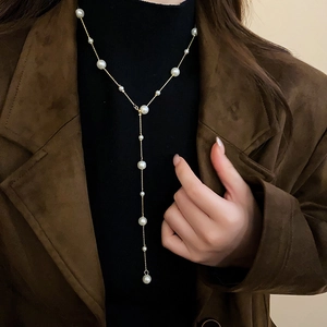 Detail of elegant gold Y-shaped necklace with multiple pearls on a black turtleneck sweater