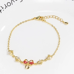 Detail view of gold bracelet featuring a red bow charm and lobster clasp closure