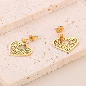 Detailed close-up of gold hollow heart earrings with leaf patterns on beige stone