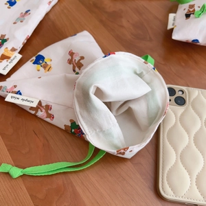 Cream drawstring canvas storage bag with colorful bear print on a wooden desk