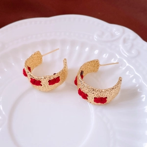 Detailed view of vintage gold C-shaped earrings with red knit texture on a ceramic plate