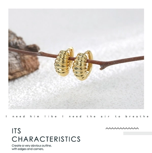 Close-up of gold croissant hoop earrings with ribbed texture on dry branches