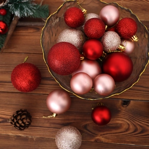 Close-up of assorted red and gold Christmas baubles in a textured glass bowl on wood