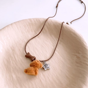 Detailed close-up of brown flocked puppy pendant and silver star charm on woven rope