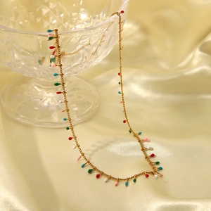 Detail of gold tassel chain necklace with colorful enamel charms on silk background