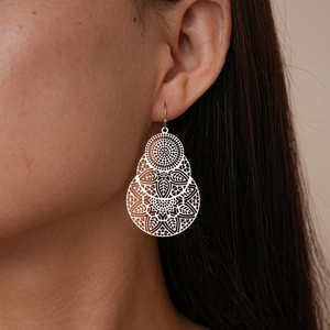 Gros plan d'une boucle d'oreille fleur argentée évidée portée avec motifs floraux délicats