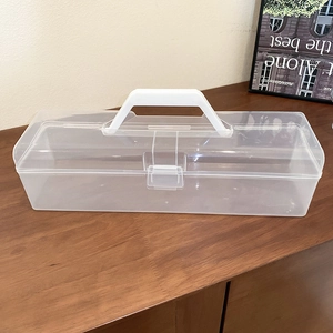 Macro shot of rectangular clear plastic jewelry box with white handle on wooden surface