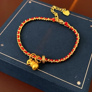 Détail du bracelet tressé rouge avec breloques calebasse dorée et petit cœur