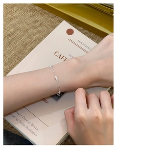 Detailed shot of an S925 silver flower bracelet worn on a wrist with a soft book background