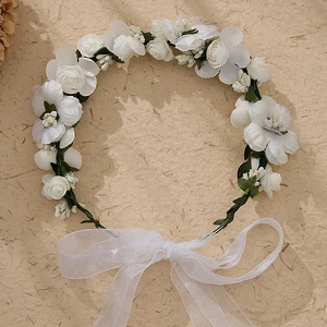 Close-up of a white floral crown with silk ribbons on a beige textured paper background