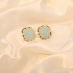 Detail of square gold-rimmed stud earrings with light blue marble texture on silk