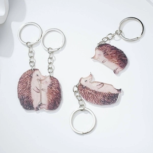 Close-up of matching wooden-style acrylic otter couple keychains on white background