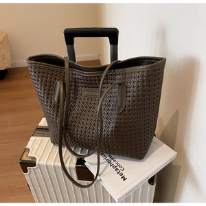 Detail of dark brown woven tote bag on white suitcase with a decorative book