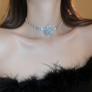Close-up of a silver rhinestone rose necklace worn by a model in warm lighting