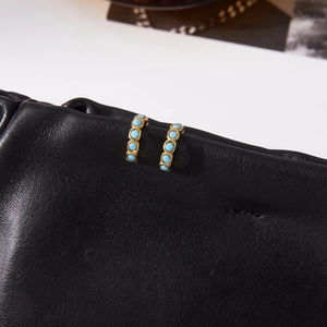 Macro shot of gold stainless steel hoop earrings with inlaid turquoise stones on black leather