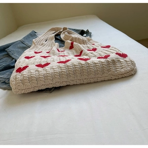 Detalle de la textura de punto de un bolso de crochet crema con motivos de corazones rojos