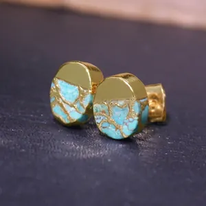 Macro view of gold mirror metal and turquoise stone round stud earrings on black surface