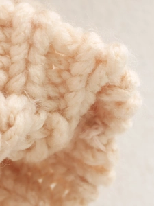 Macro shot of soft cream chunky knit cardigan showing thick yarn texture and plush feel