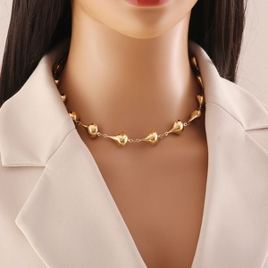 Close-up of golden metallic teardrop pendant necklace worn by model in beige suit