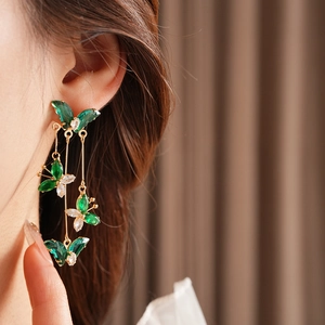 Détail de boucles d'oreilles pendantes dorées avec papillons en zircons verts et clairs