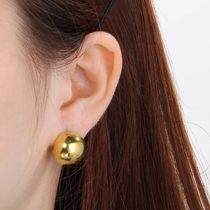 Close-up of a minimalist golden half-sphere earring worn on the ear showing polished finish