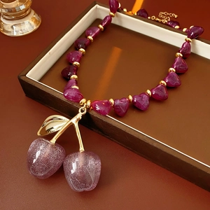 Macro detail of purple glitter cherry pendant and heart beads on a gold necklace