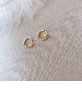 Close-up of gold huggie earrings featuring small white pearls on a soft linen surface