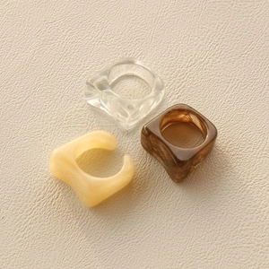 Three minimalist resin rings in clear, amber brown, and cream yellow on beige leather