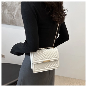Close-up of white quilted crossbody bag with gold chain strap on a model's shoulder