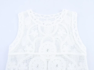 Dettaglio del gilet in maglia di pizzo bianco con motivi floreali e dettagli di frange