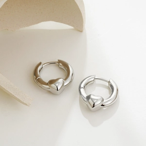 Polished silver heart hoop earrings with a 3D heart charm on a minimalist display
