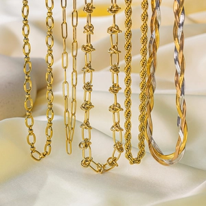 Multiple styles of 18k gold Cuban and herringbone necklaces on beige silk background