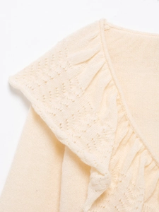 Detailed close-up of eyelet knit pattern and ruffled neckline on cream sweater