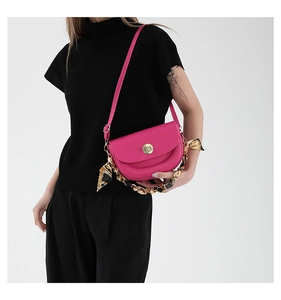 Detail of rose red saddle bag with gold clasp and decorative silk scarf chain strap
