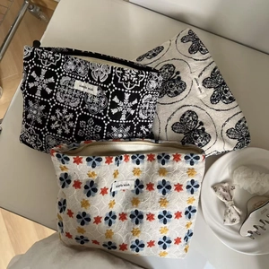 Detailed close-up of three embroidered canvas pouches with floral and butterfly patterns