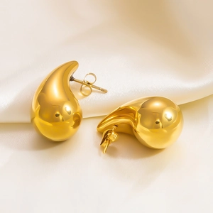 Close-up of golden teardrop stud earrings on cream silk fabric with elegant lighting