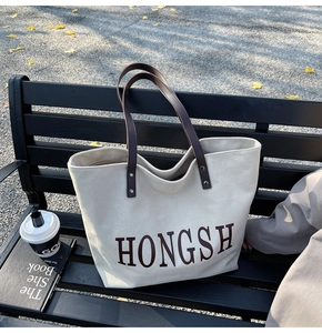 Detailed texture of off-white canvas tote bag with brown leather handles on park bench