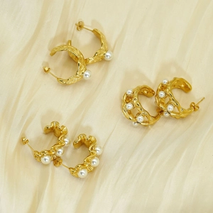 Three pairs of elegant gold titanium earrings with white pearls on a beige silk background