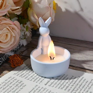 Blauwe konijn geurkaars met twee pitten brandend op een houten tafel met bloemen