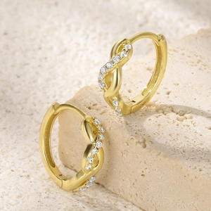 Close-up of gold infinity twist huggie earrings with white zircon stone inlay